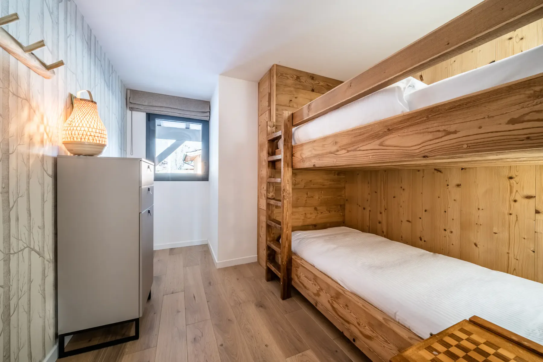 Un dormitorio compacto con literas de madera, un refrigerador pequeño y una ventana.
