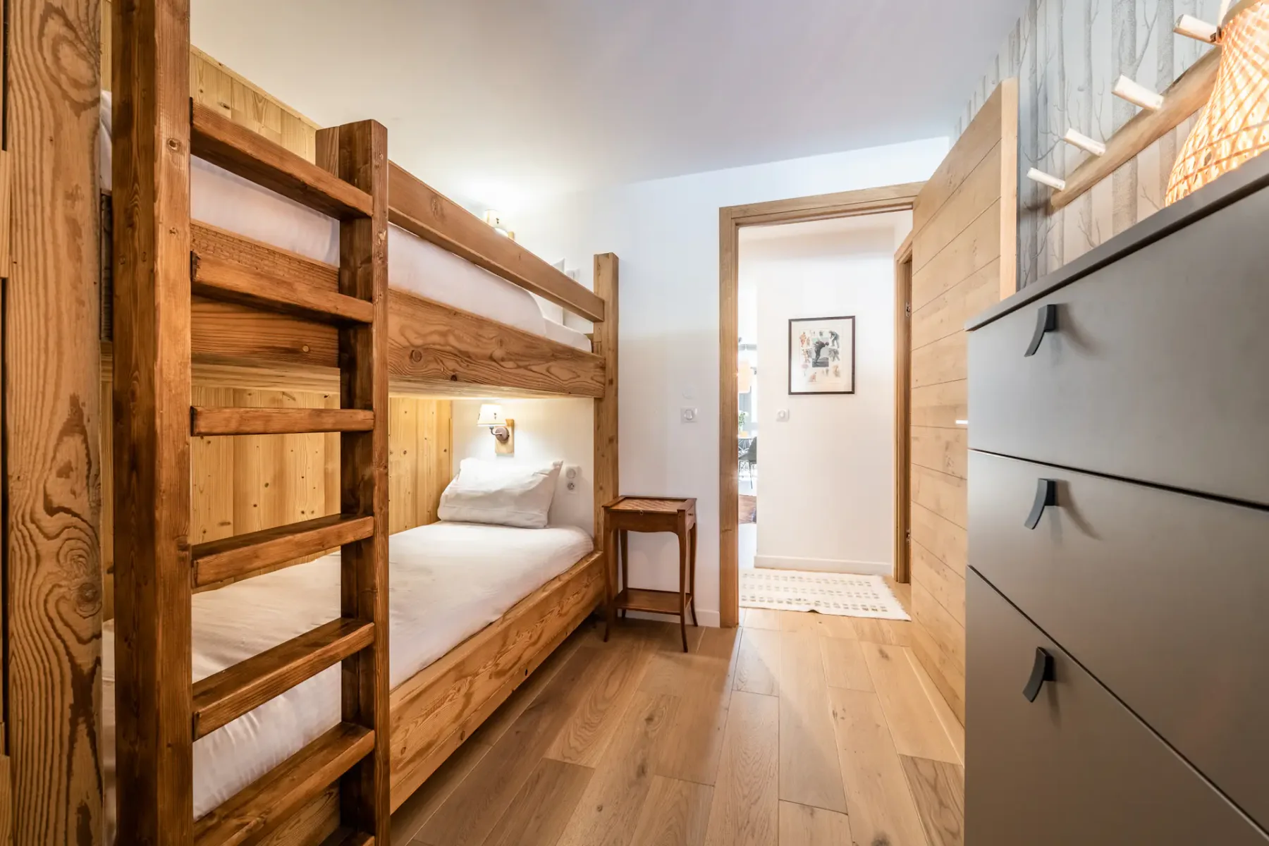 Zona de descanso con una litera, una escalera de madera y una cómoda.