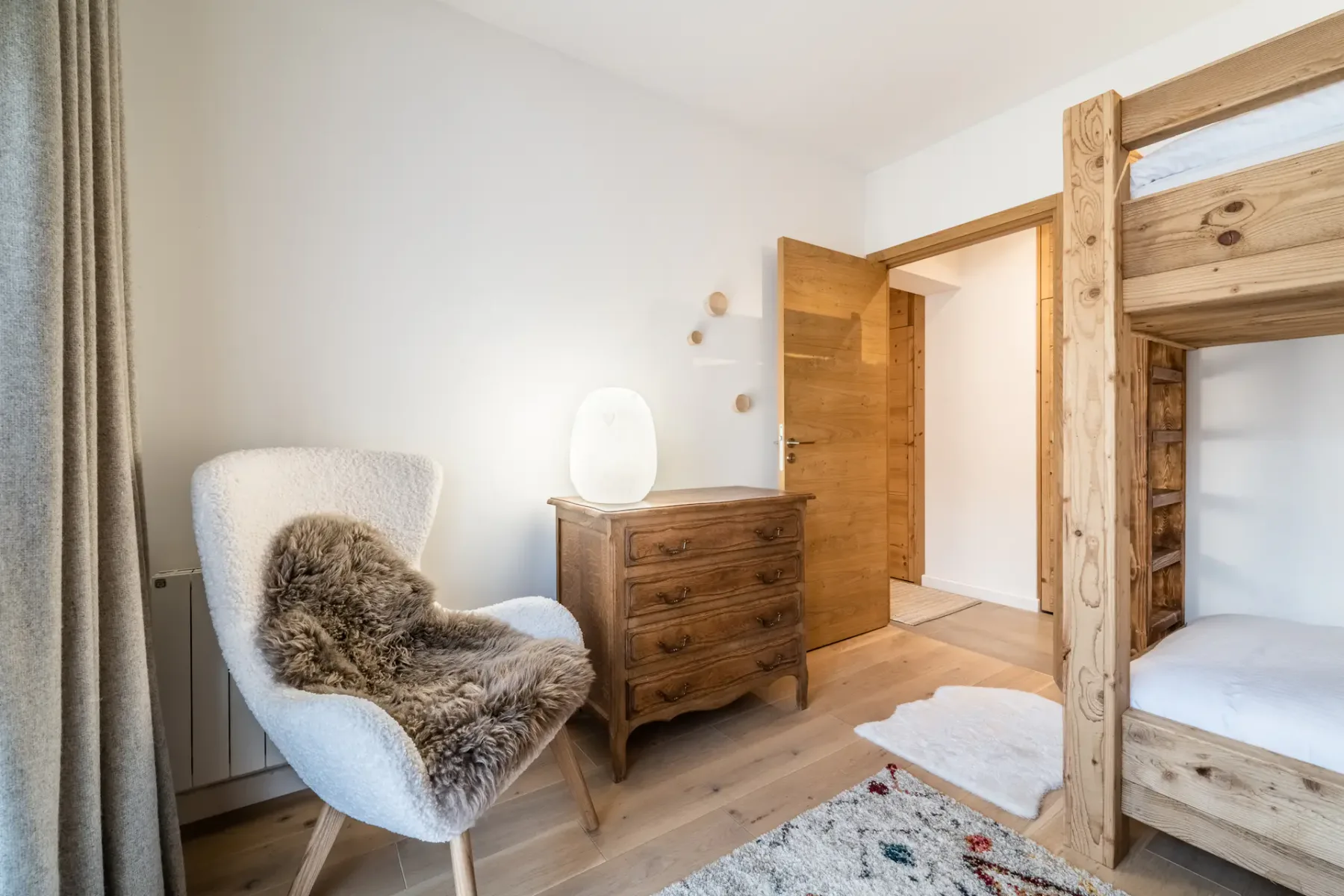 Una zona de estar en un dormitorio con una cómoda de madera, un sillón y una litera.