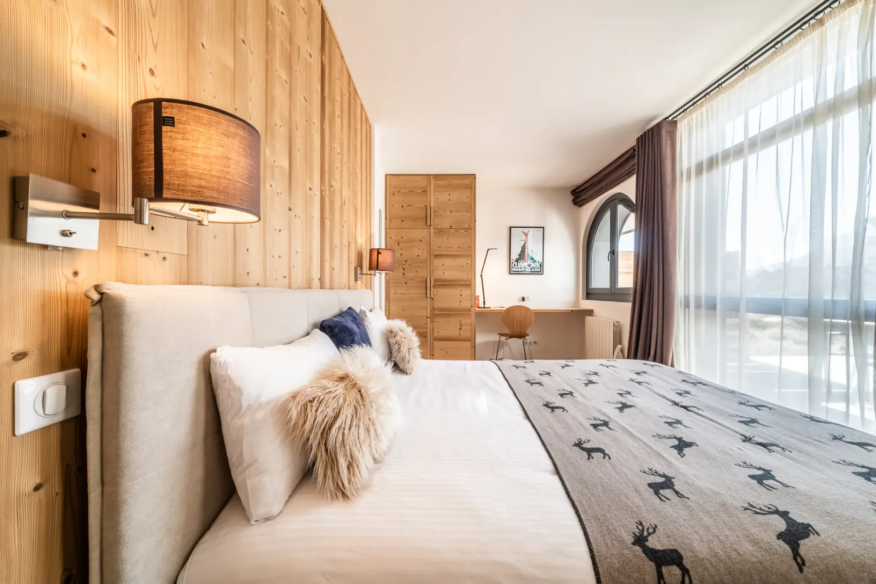 Un dormitorio con una cama bien arreglada y ventanas grandes.