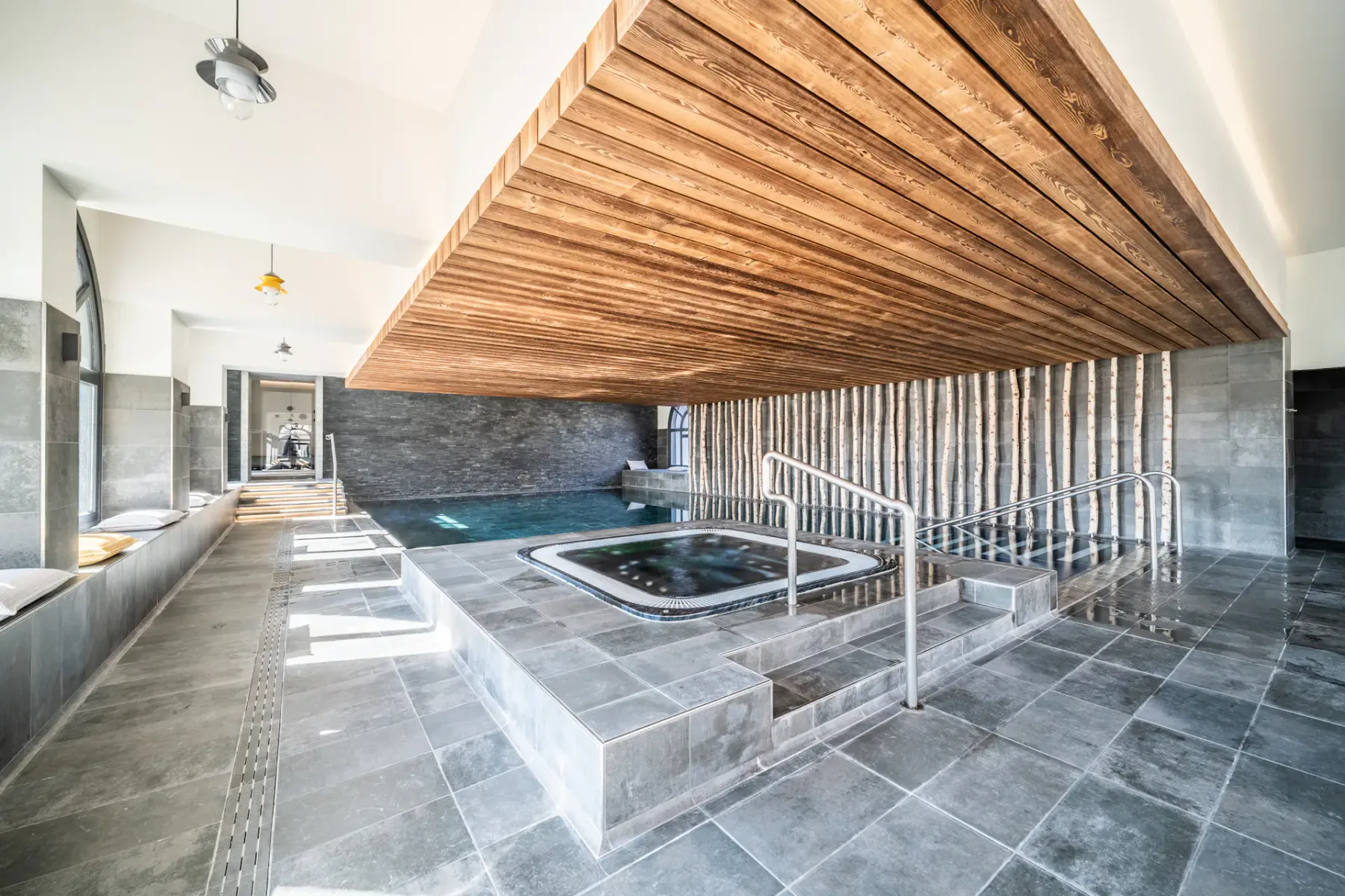 Una piscina cubierta y una bañera de hidromasaje están bajo un techo de paneles de madera.