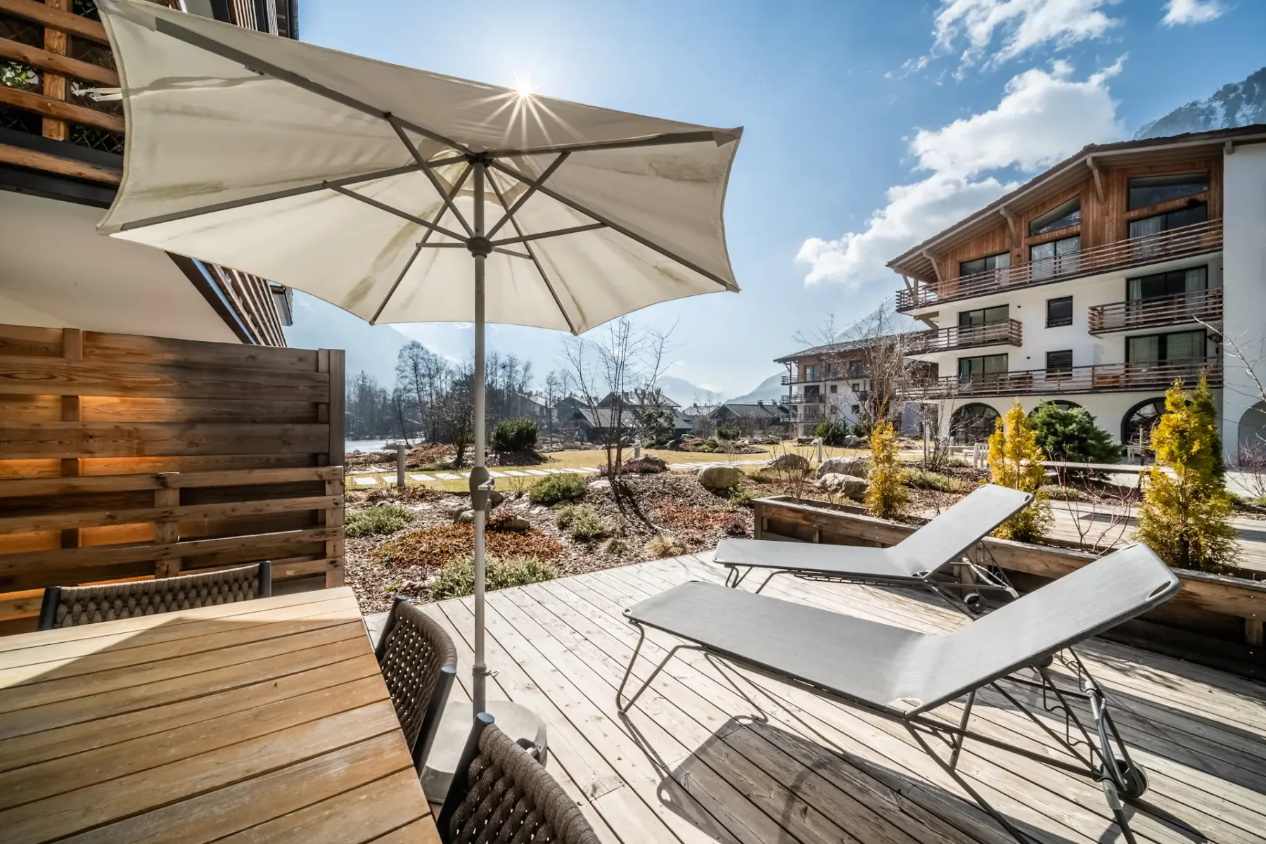 Un patio soleado al aire libre con asientos, una sombrilla grande y vistas a las montañas.