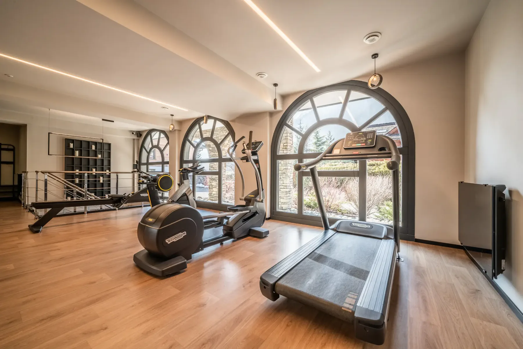 Una sala de ejercicios con cintas de correr y equipo junto a grandes ventanas arqueadas.
