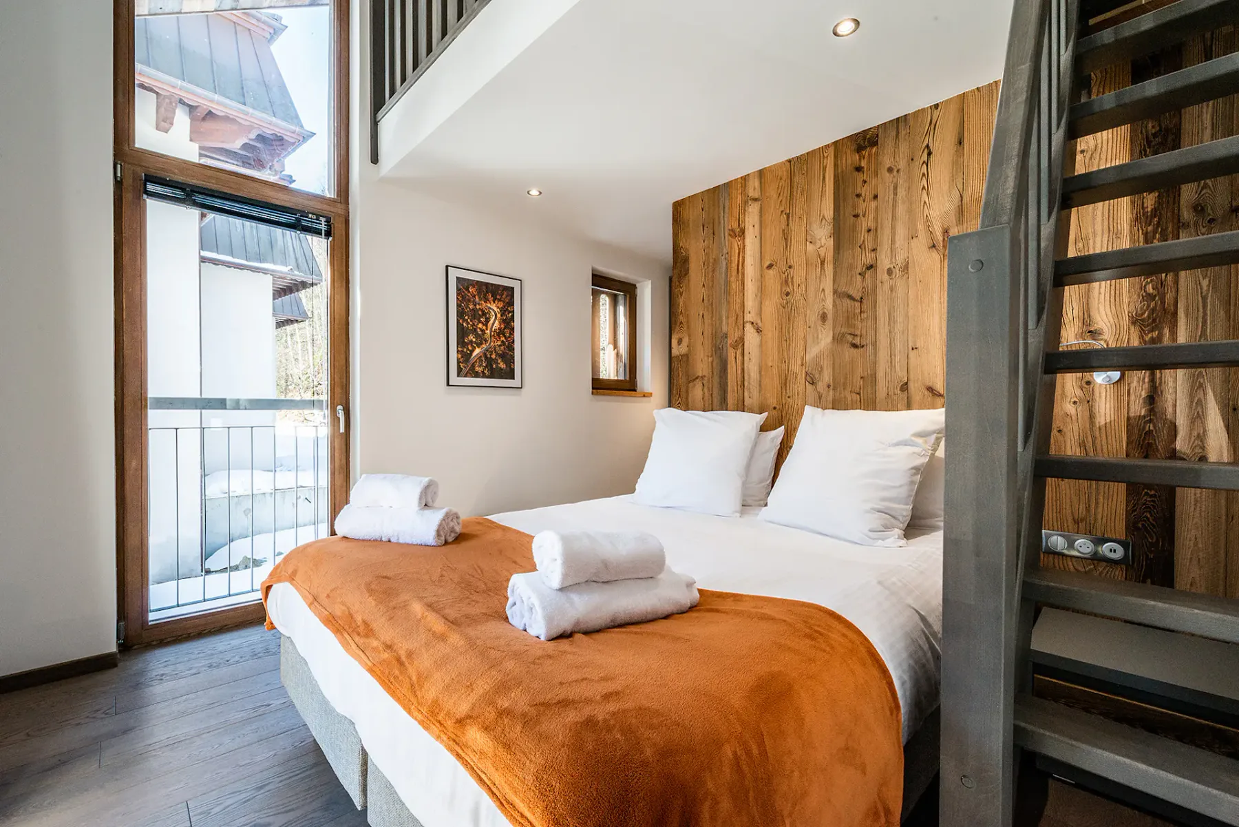 Un dormitorio con una cama vestida con ropa blanca y una manta naranja.
