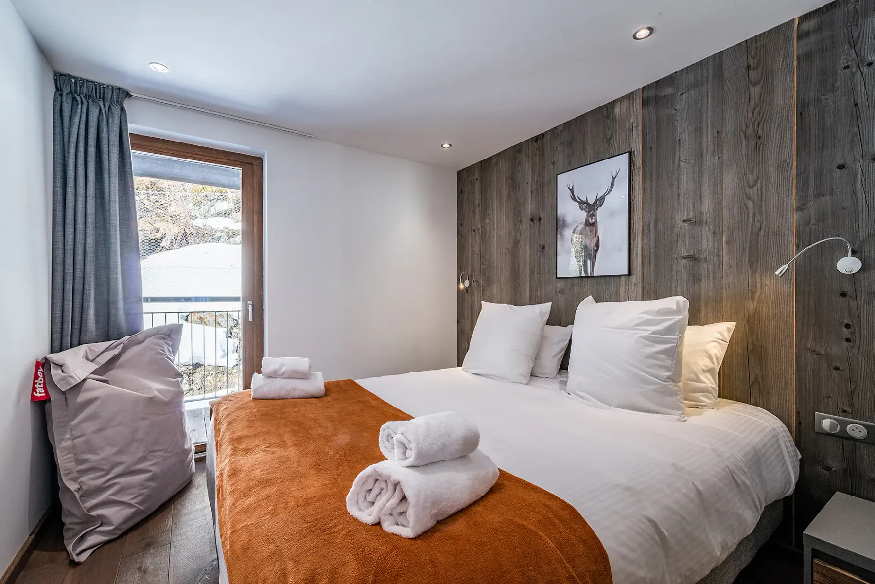 Un dormitorio con una cama tendida, toallas dobladas y una pared revestida de madera.