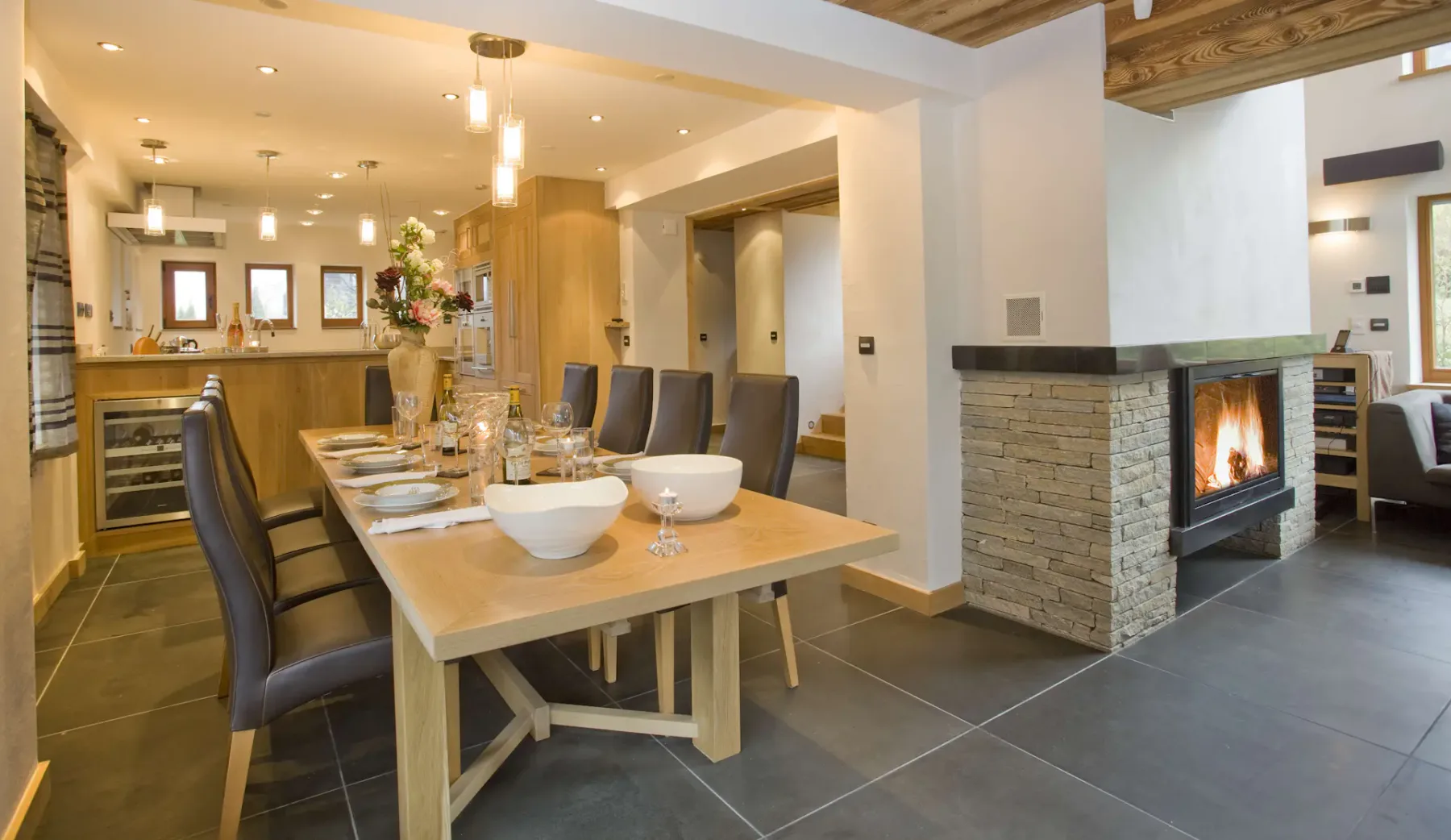Una zona abierta de comedor y cocina tiene una mesa larga y una chimenea encendida.