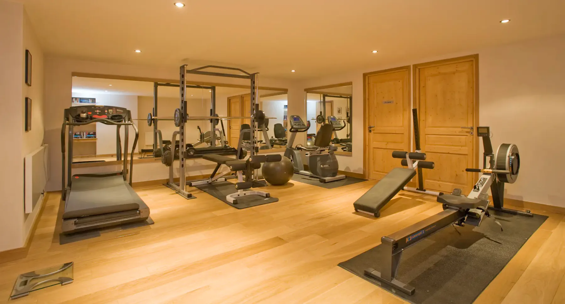 Un gimnasio en casa con equipos de ejercicio y una cinta de correr sobre suelo de madera.