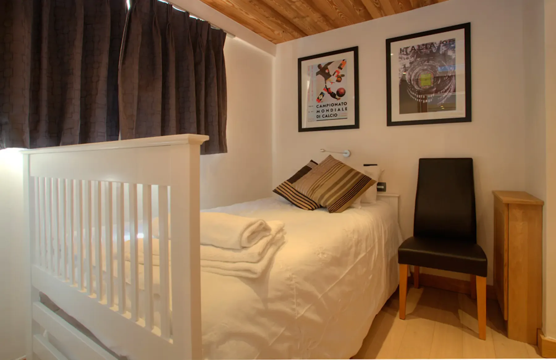 Un dormitorio compacto con una cama, cortinas oscuras y una silla.