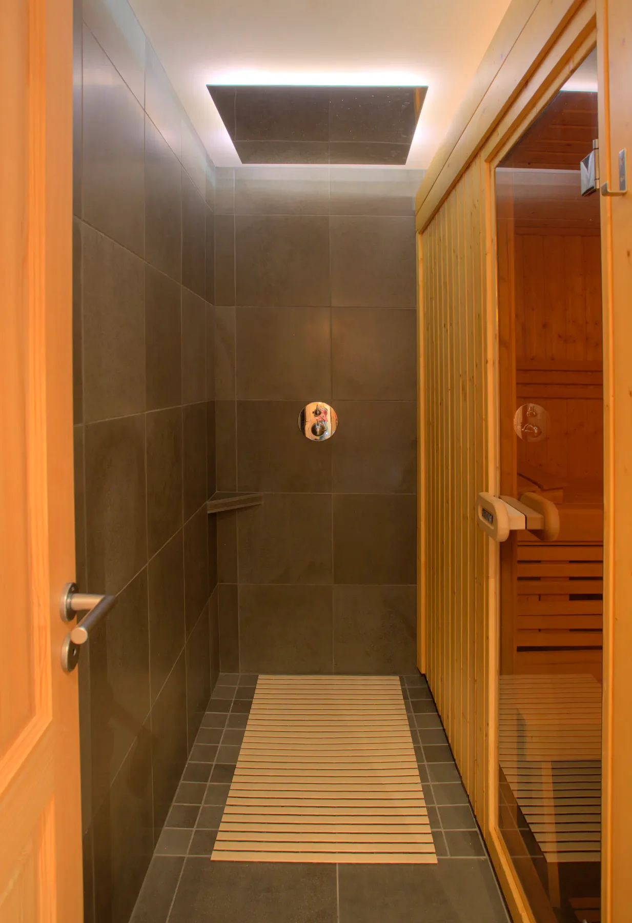 Una zona de ducha con azulejos se abre junto a una sauna de madera.