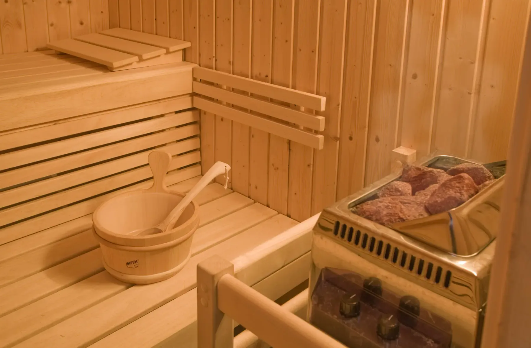 Una sauna de madera con bancos escalonados y un calentador lleno de piedras.
