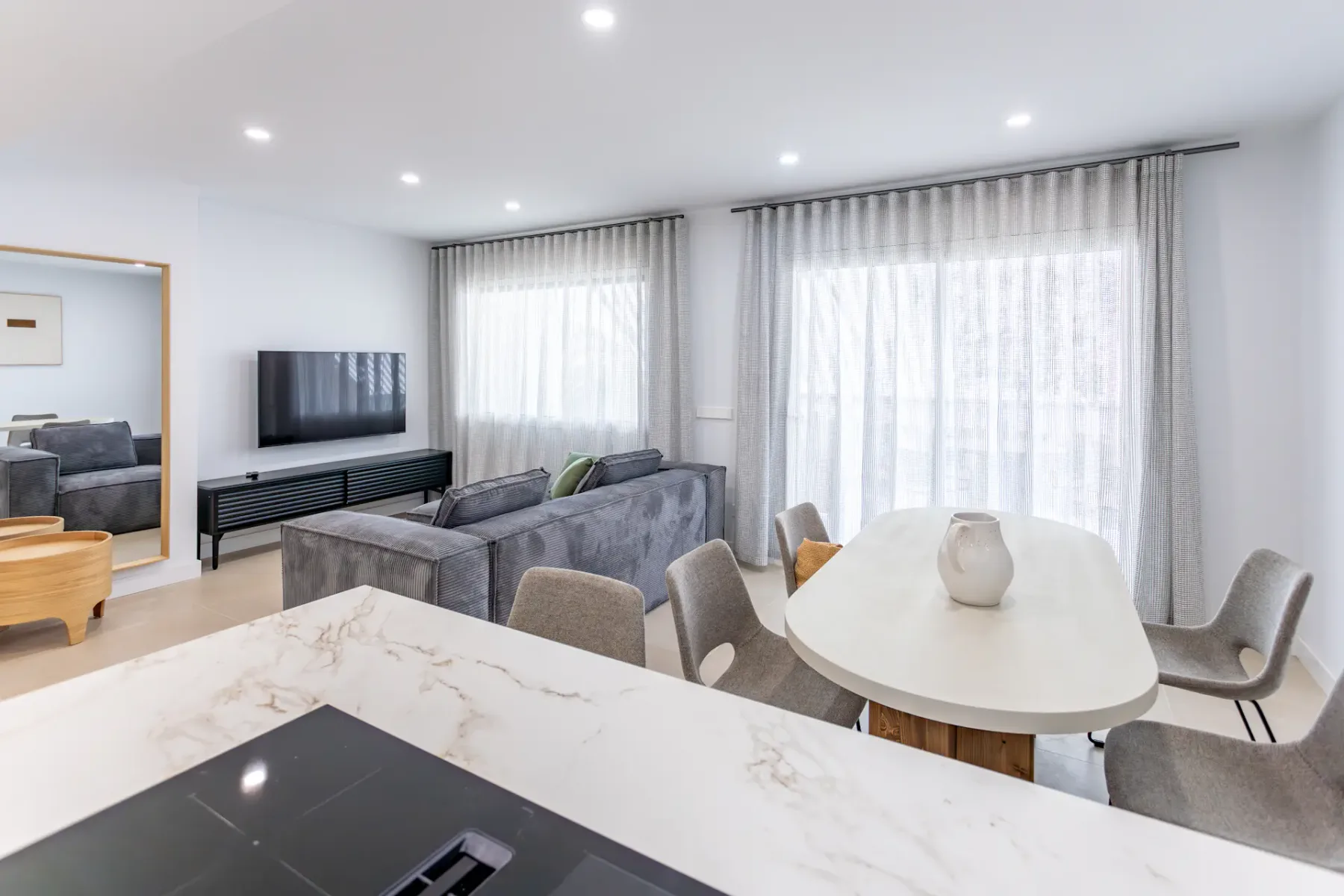 A bright open-plan living and dining room with gray seating and a white table.