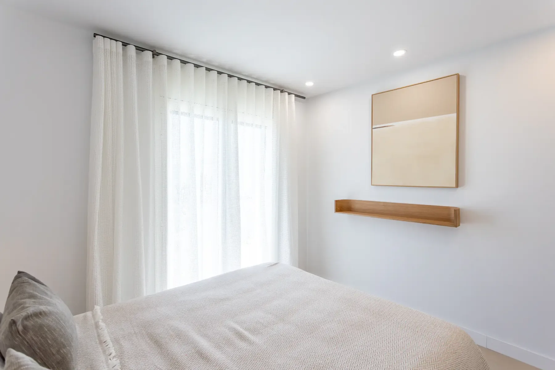 A bright bedroom with a bed beside a large curtained window.