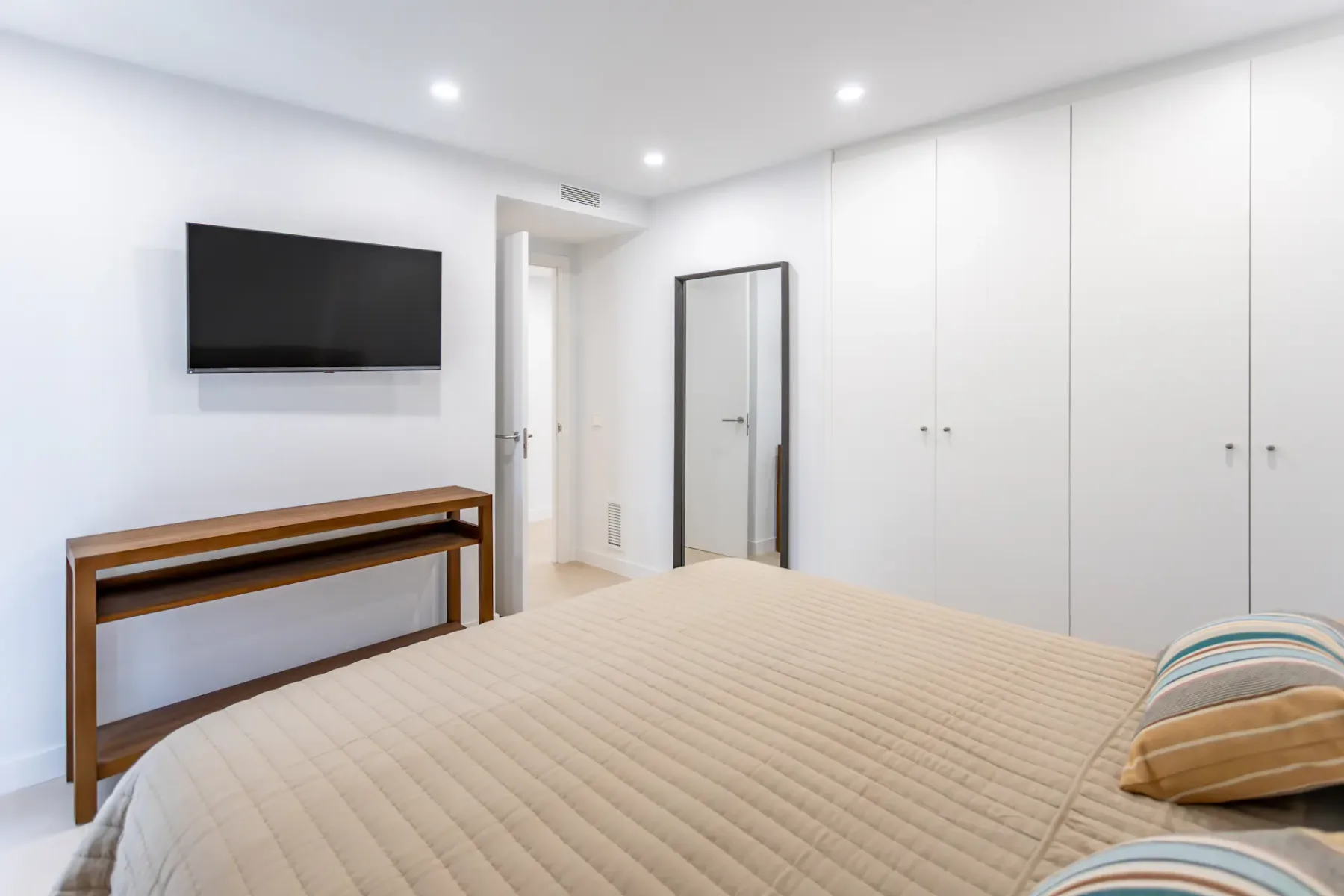A bright bedroom with a television mounted above a narrow console.