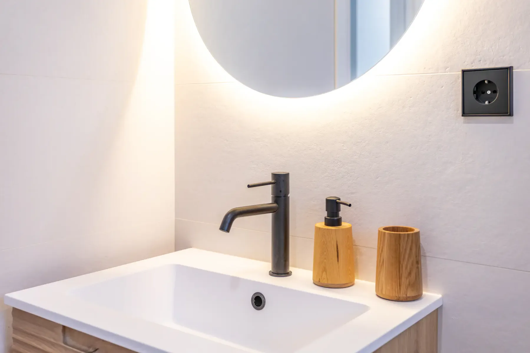 Bathroom vanity with a white sink, dark faucet, and round mirror.