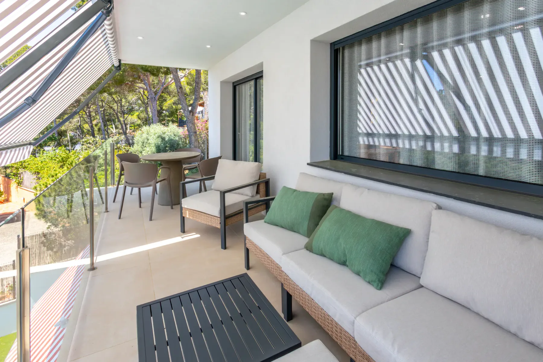 A furnished balcony with outdoor seating and a glass railing overlooks leafy trees.