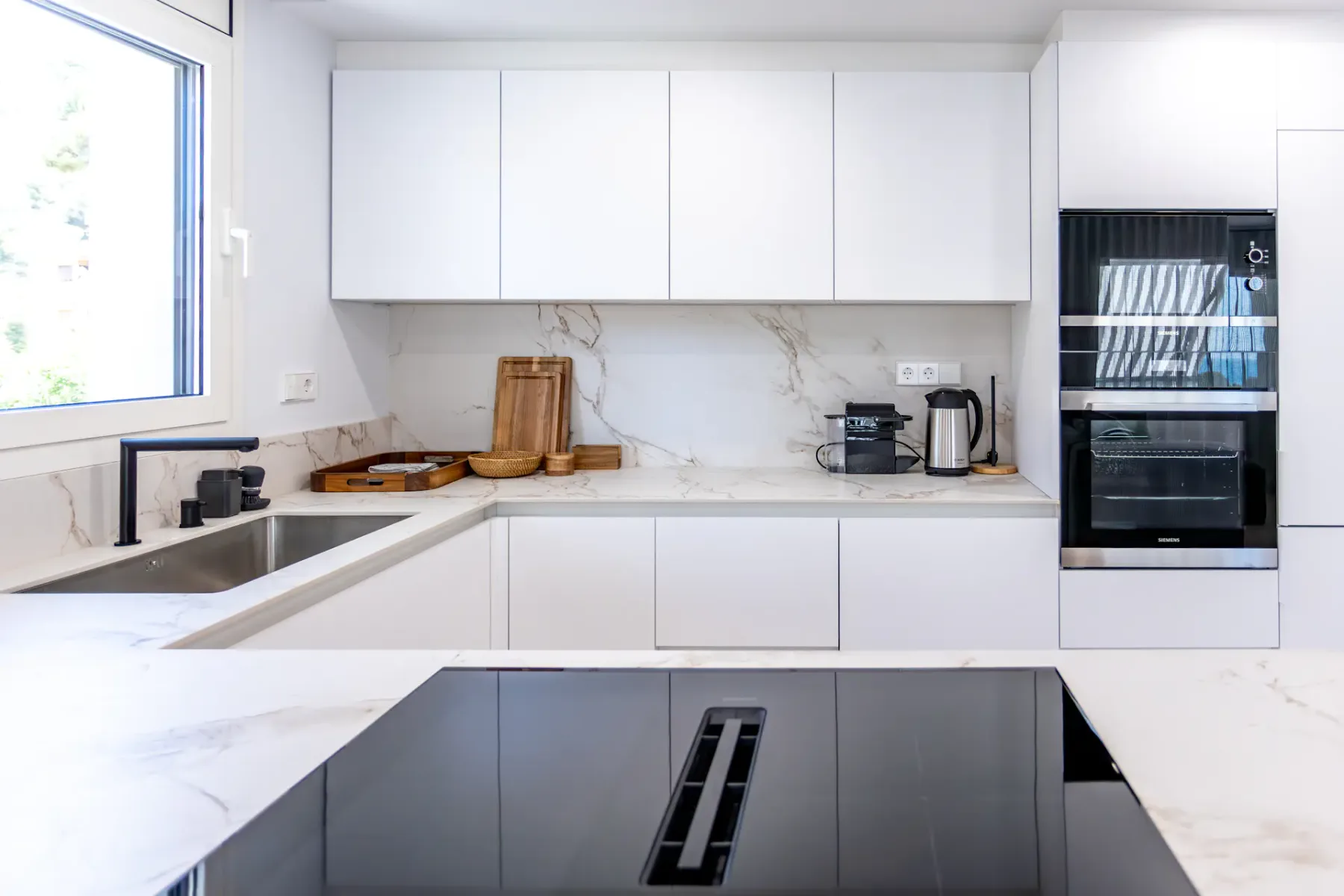 A bright modern kitchen with white cabinets and a dark cooktop.
