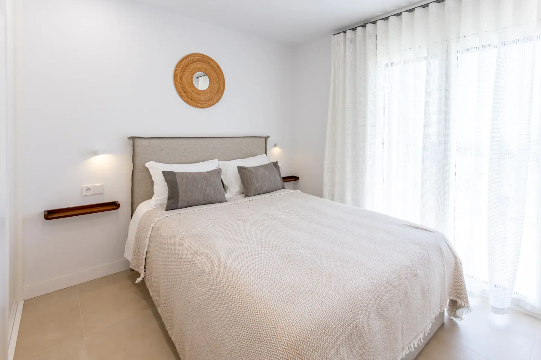 A bright bedroom with a neatly made bed and sheer curtains.