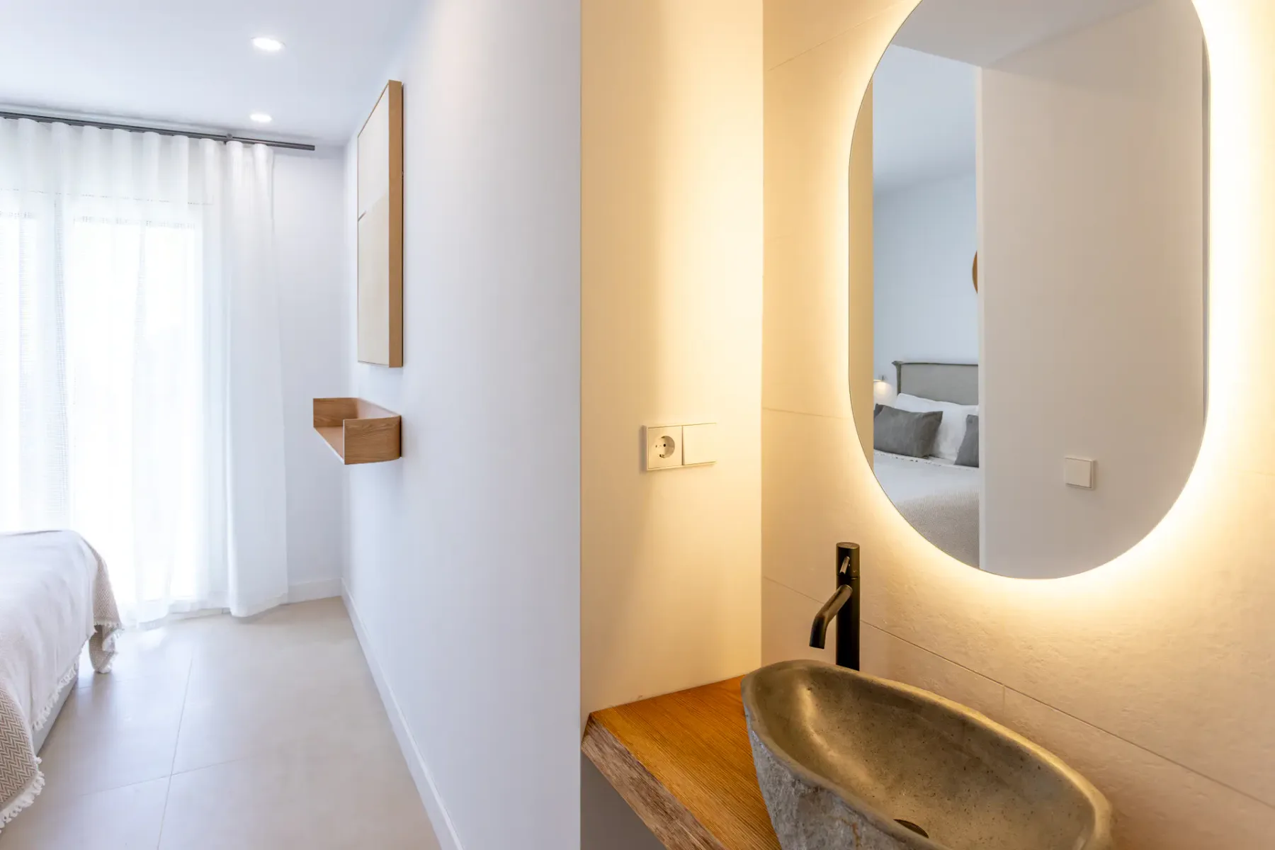 A bedroom beside a vanity with a backlit oval mirror and basin.