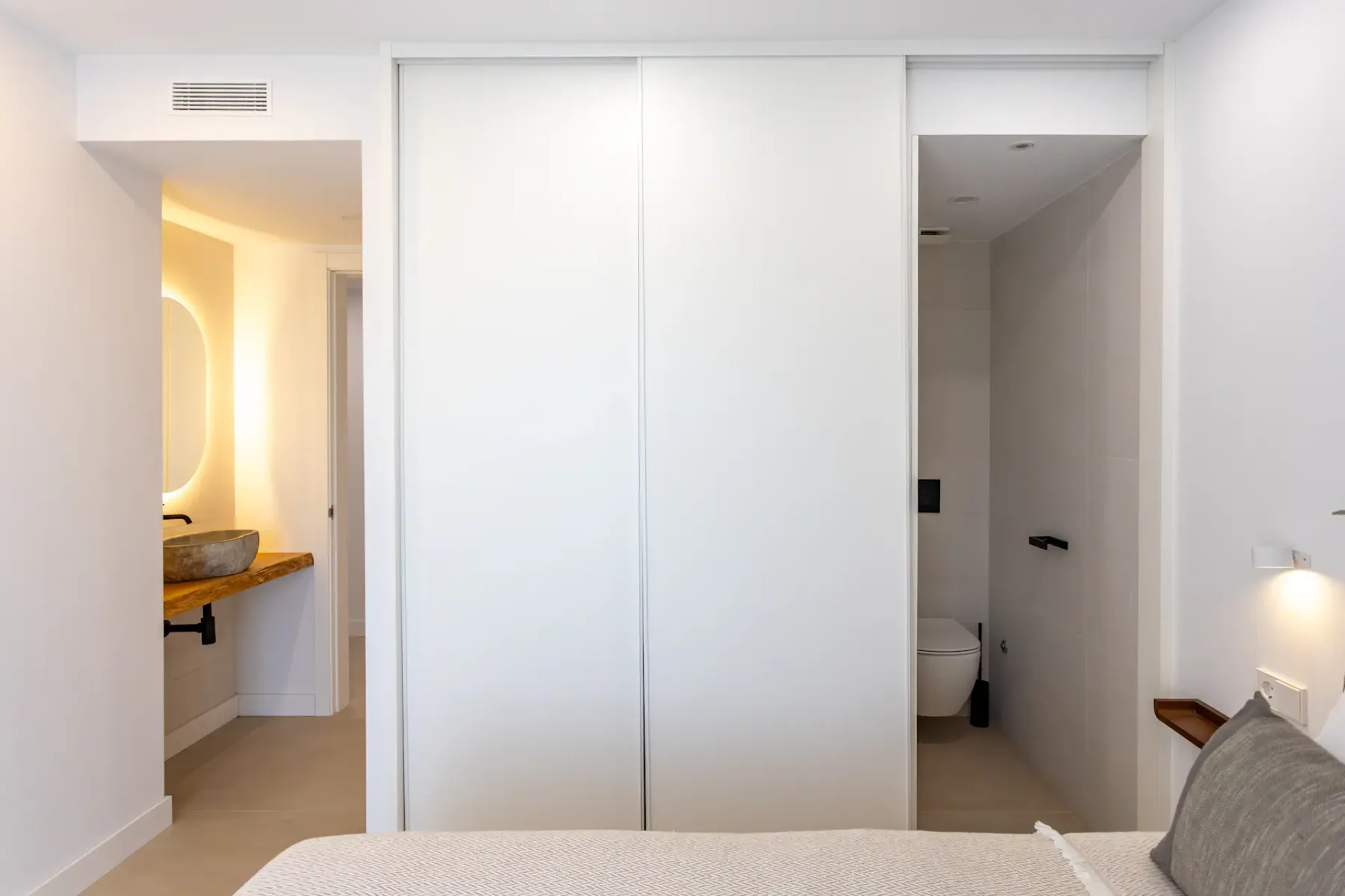 A bedroom with a bed, a washbasin area, and an open bathroom doorway.
