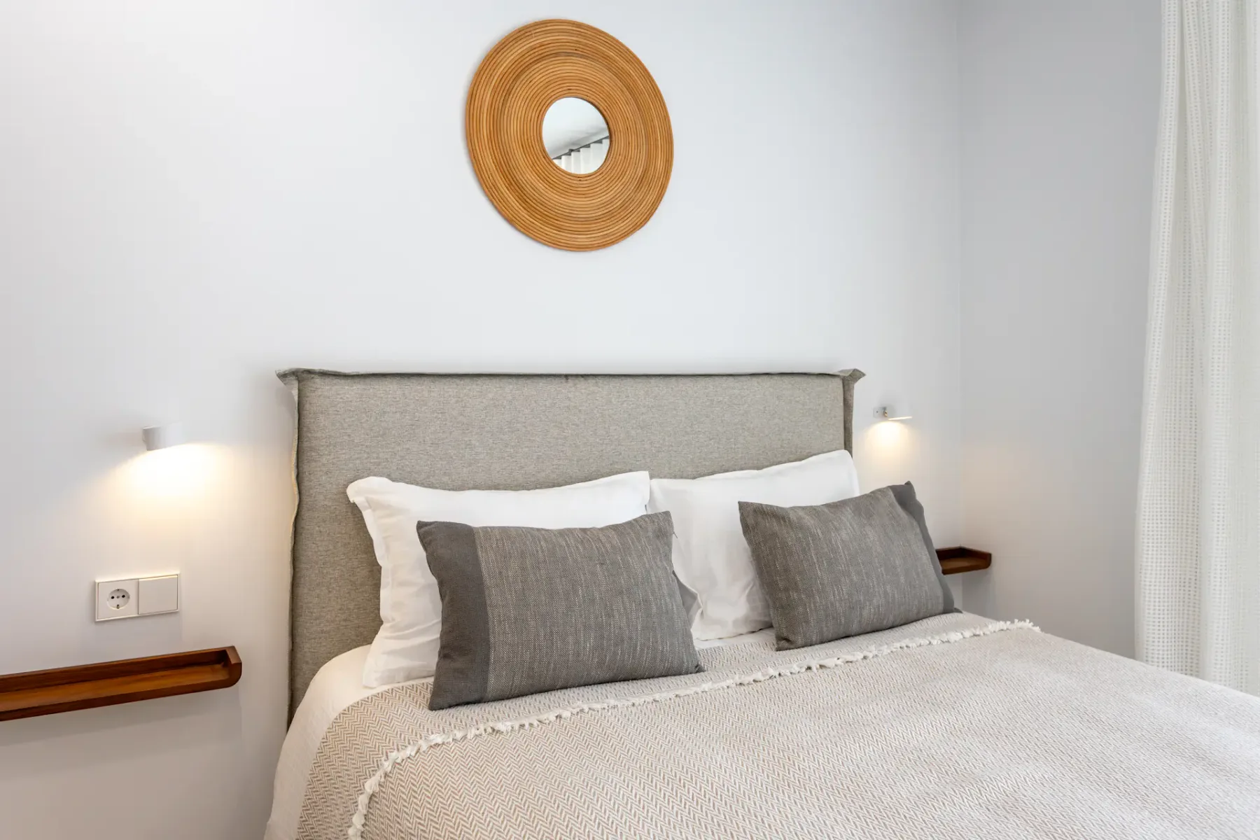 A bedroom with a neatly made bed and a round wall mirror above the headboard.