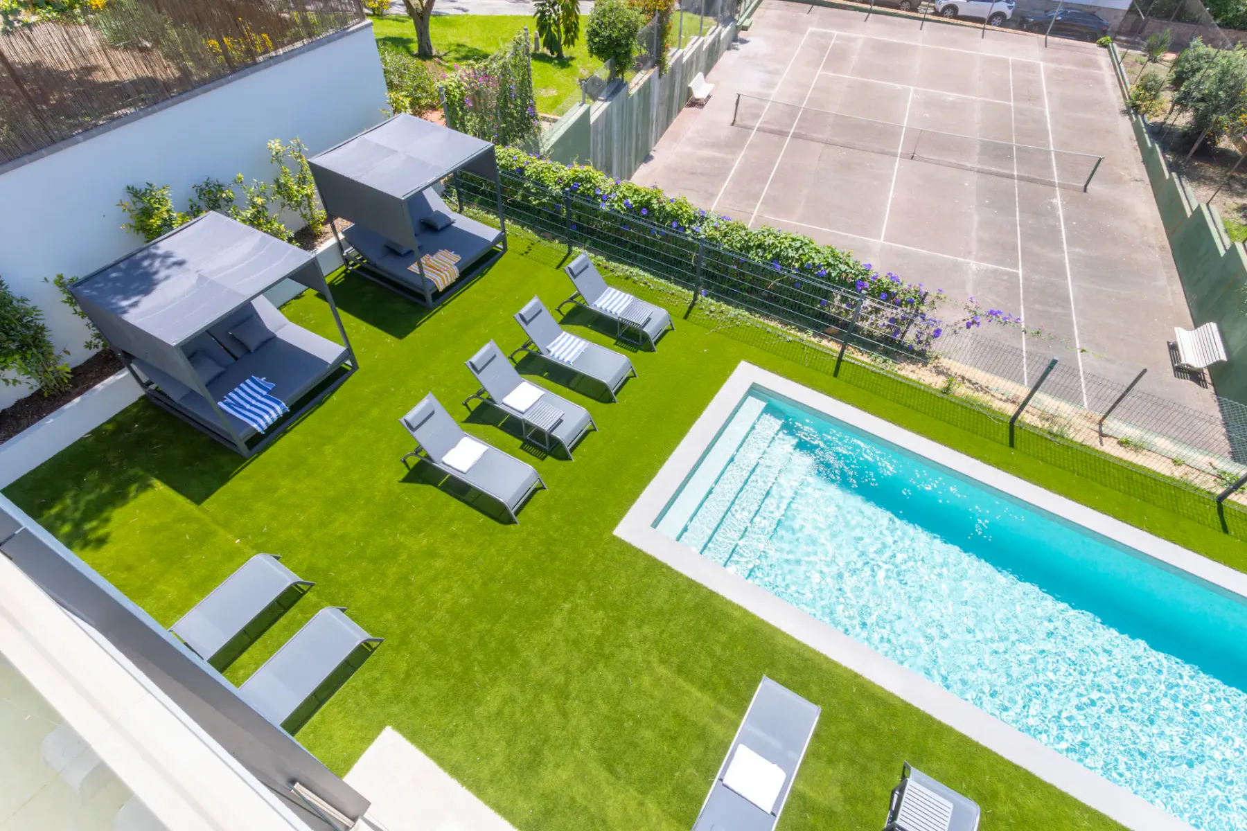 A swimming pool and lounge area sit beside a fenced sports court.