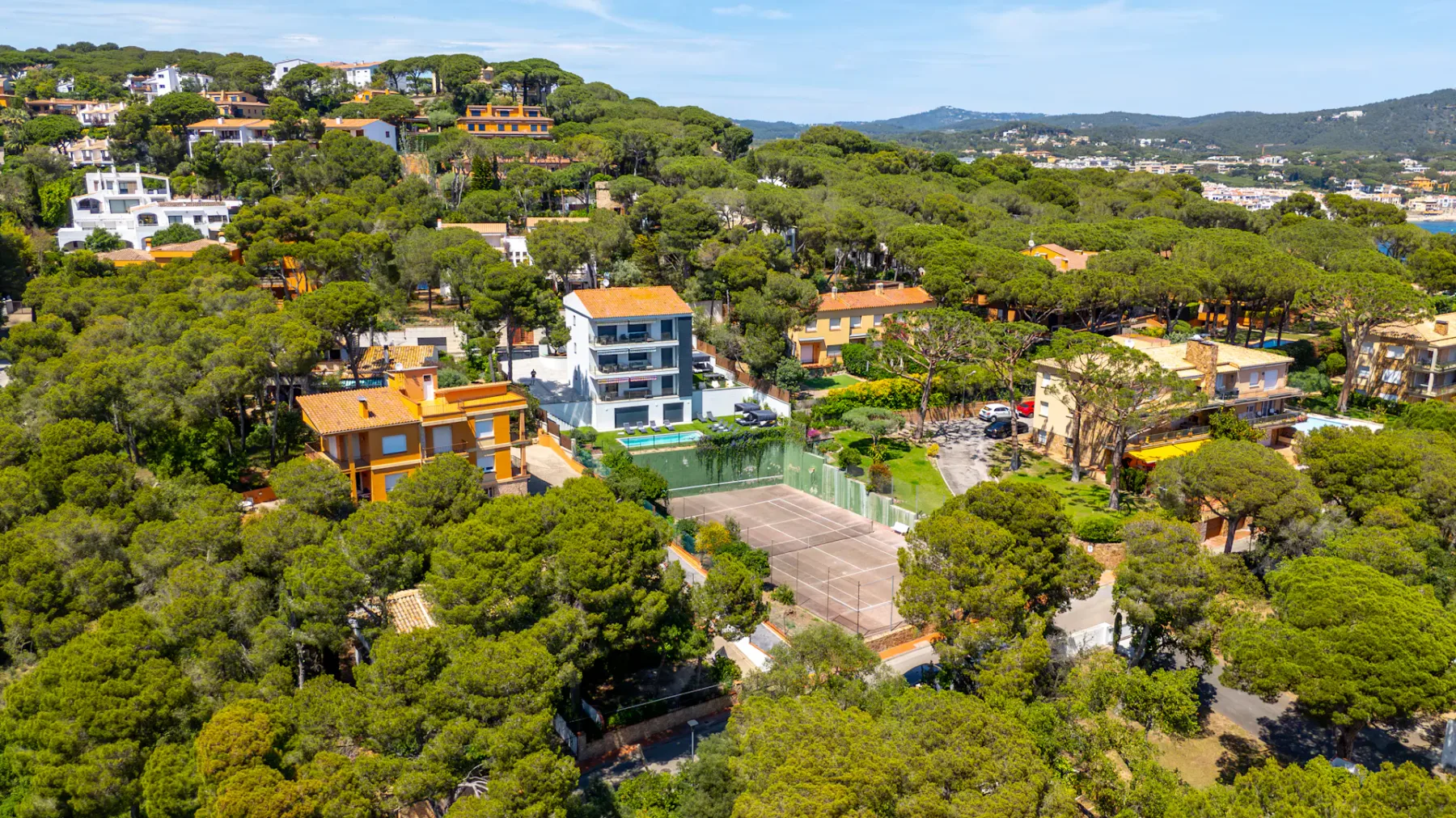 Shared amenity: Aerial view of a wooded residential area with a tennis court.