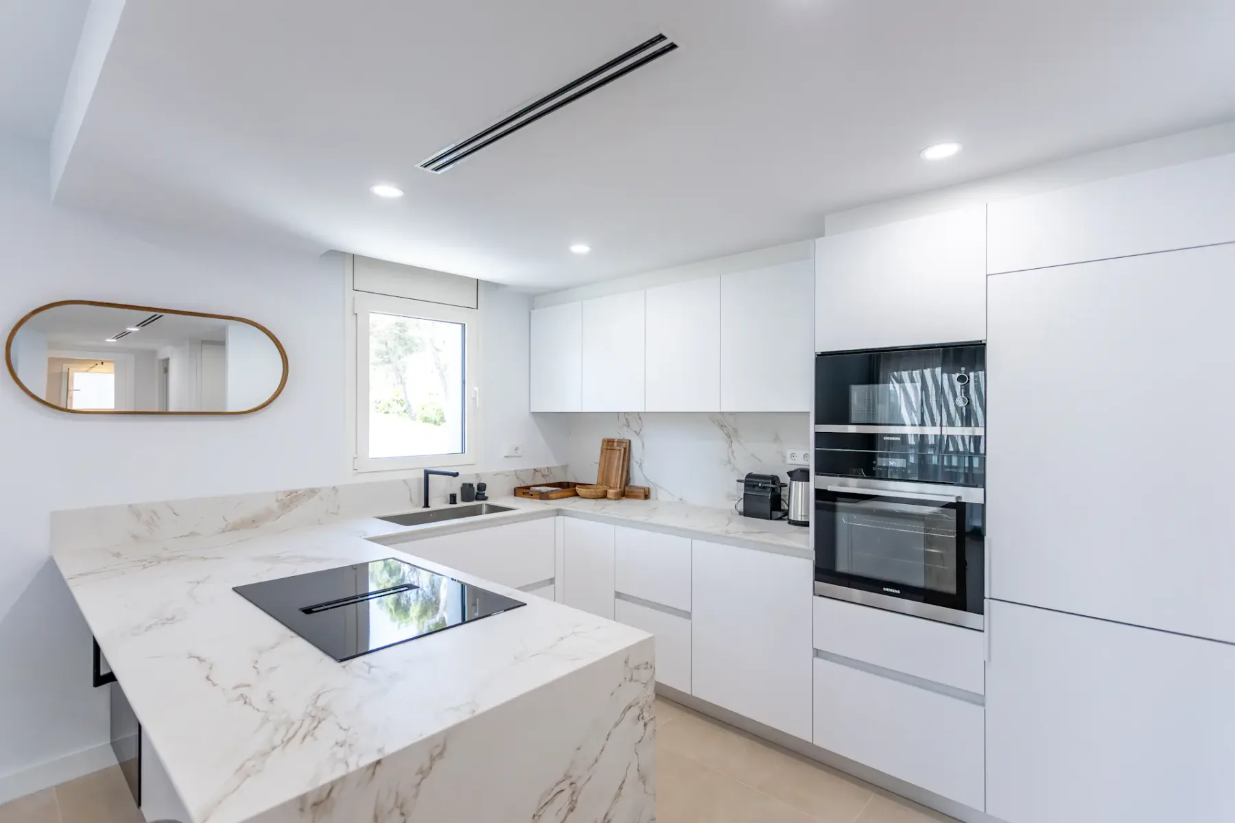 A bright modern kitchen with white cabinets and a marble-patterned island.