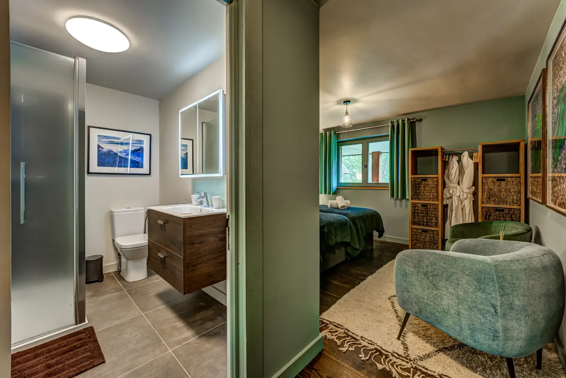 A bedroom with a green bed, curtained windows, a folding screen, and an upholstered chair beside an open bathroom.