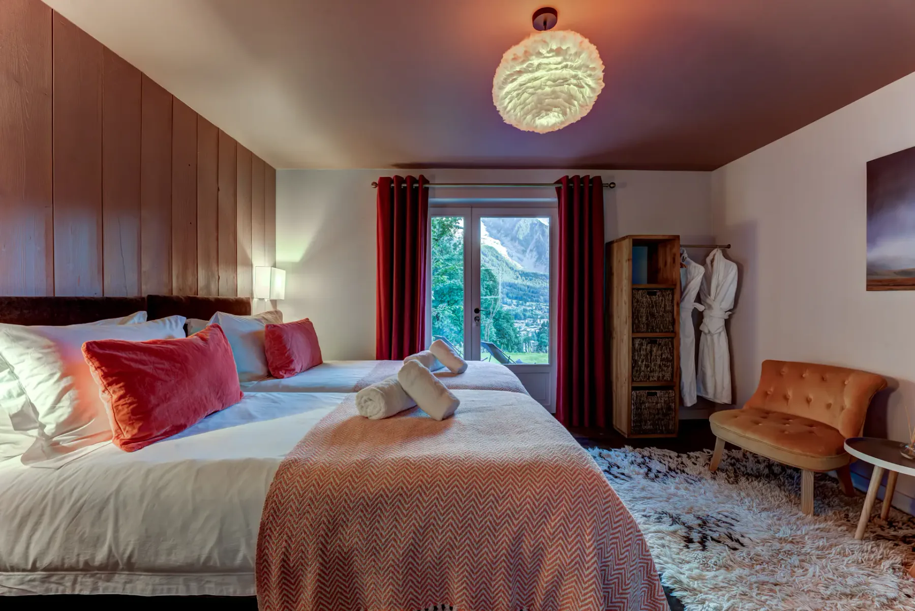 A bedroom with a large bed, red curtains, and a window overlooking a mountain landscape.