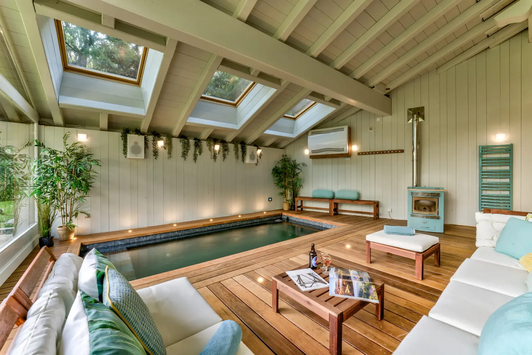 An indoor pool sits beside a wood-deck lounge with sofas, skylights, and exposed ceiling beams.