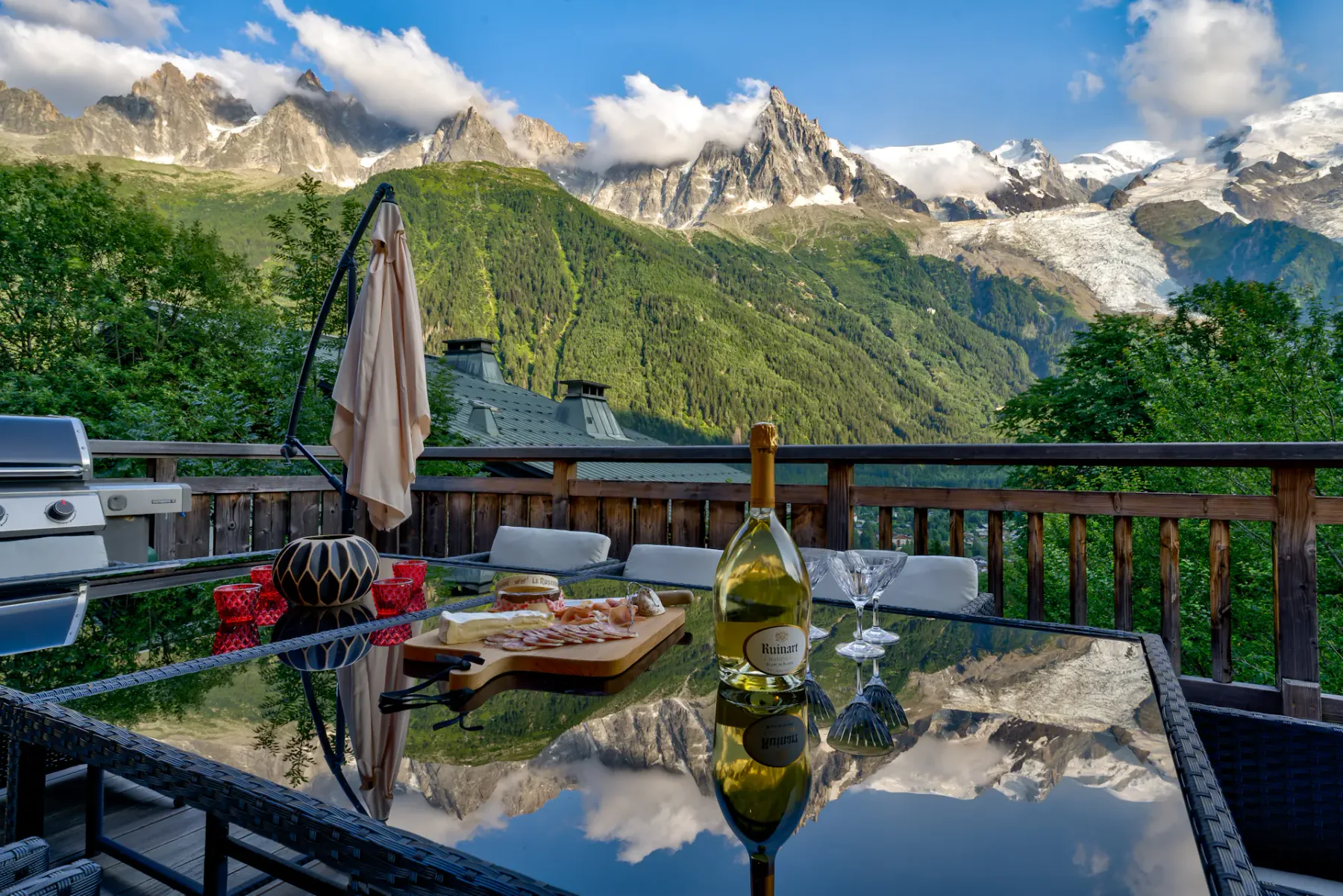 Mountain terrace with a glass table set for a meal, outdoor seating, and a view of snow-covered peaks.
