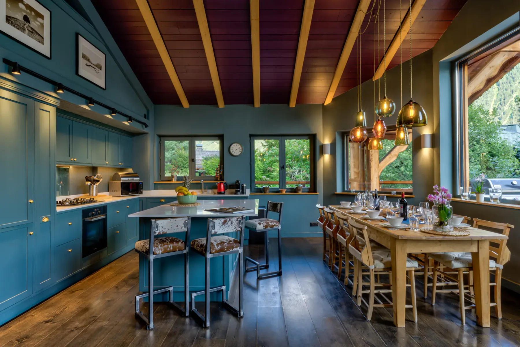 A spacious kitchen and dining area features blue cabinetry, a central island, wooden tables, and pendant lights.