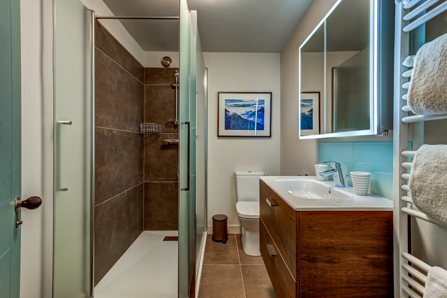 A modern bathroom features a glass-enclosed shower, a wooden vanity, and a towel warmer.