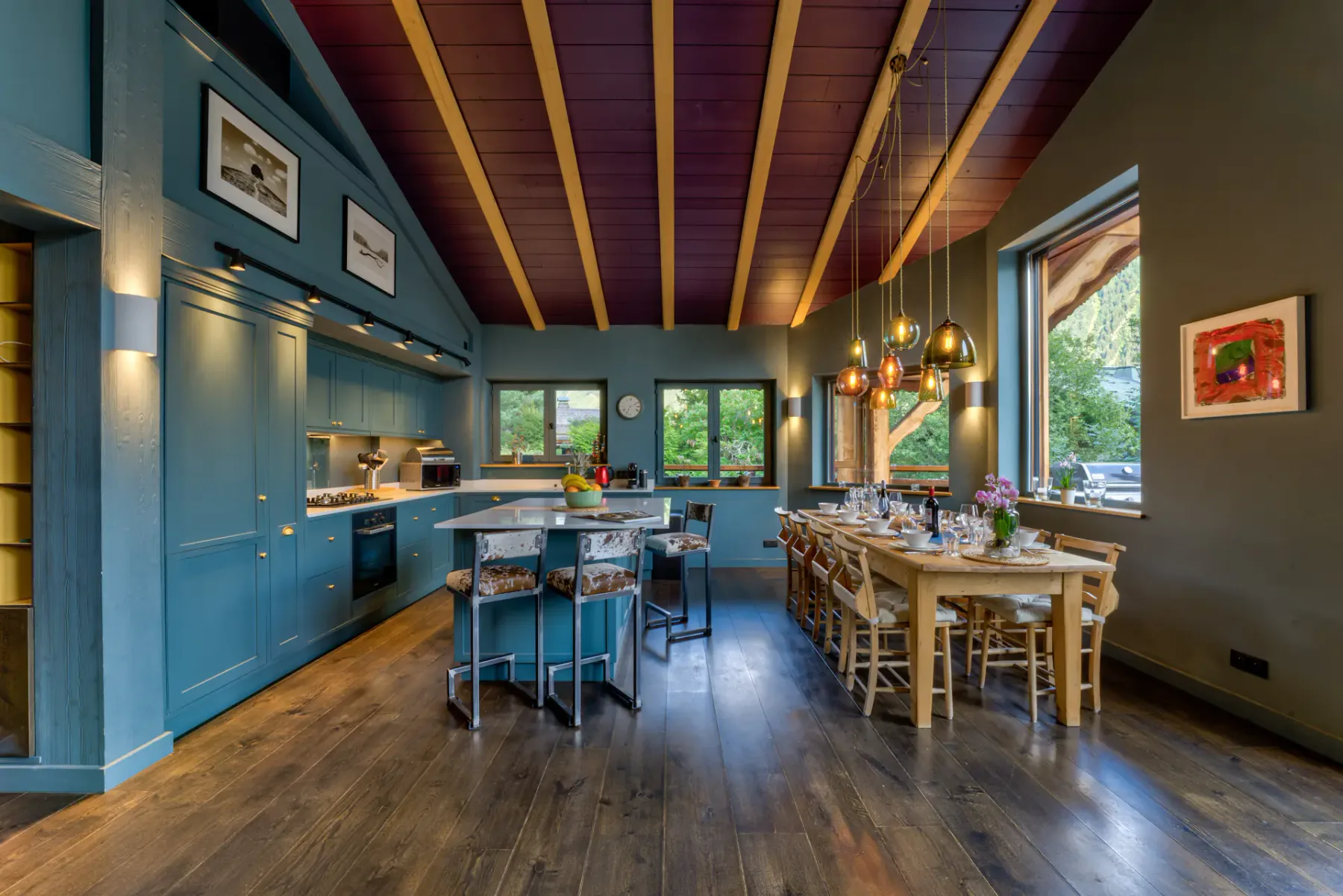 A spacious dining room with a long wooden table, blue cabinetry, and exposed ceiling beams.