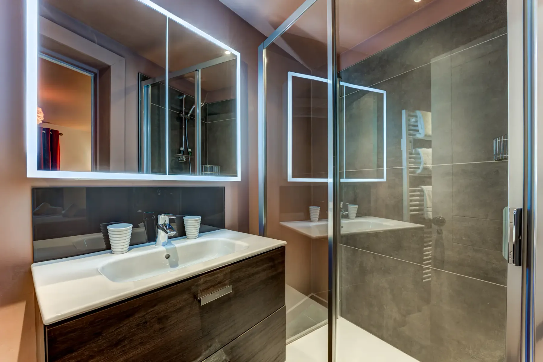 A modern bathroom with a long double sink, mirrored cabinets, and a glass-enclosed shower.