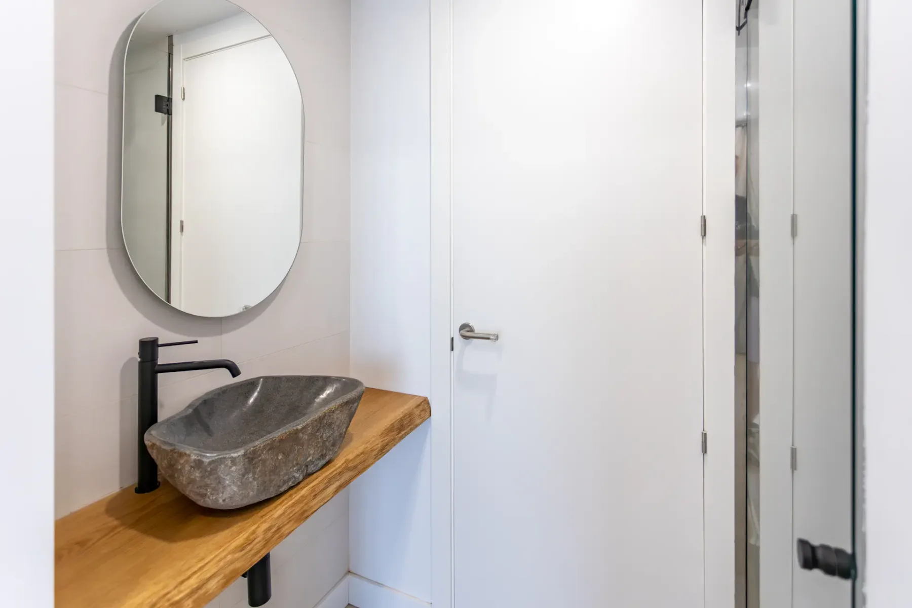A bathroom vanity has a stone basin, wooden countertop, and oval mirror.