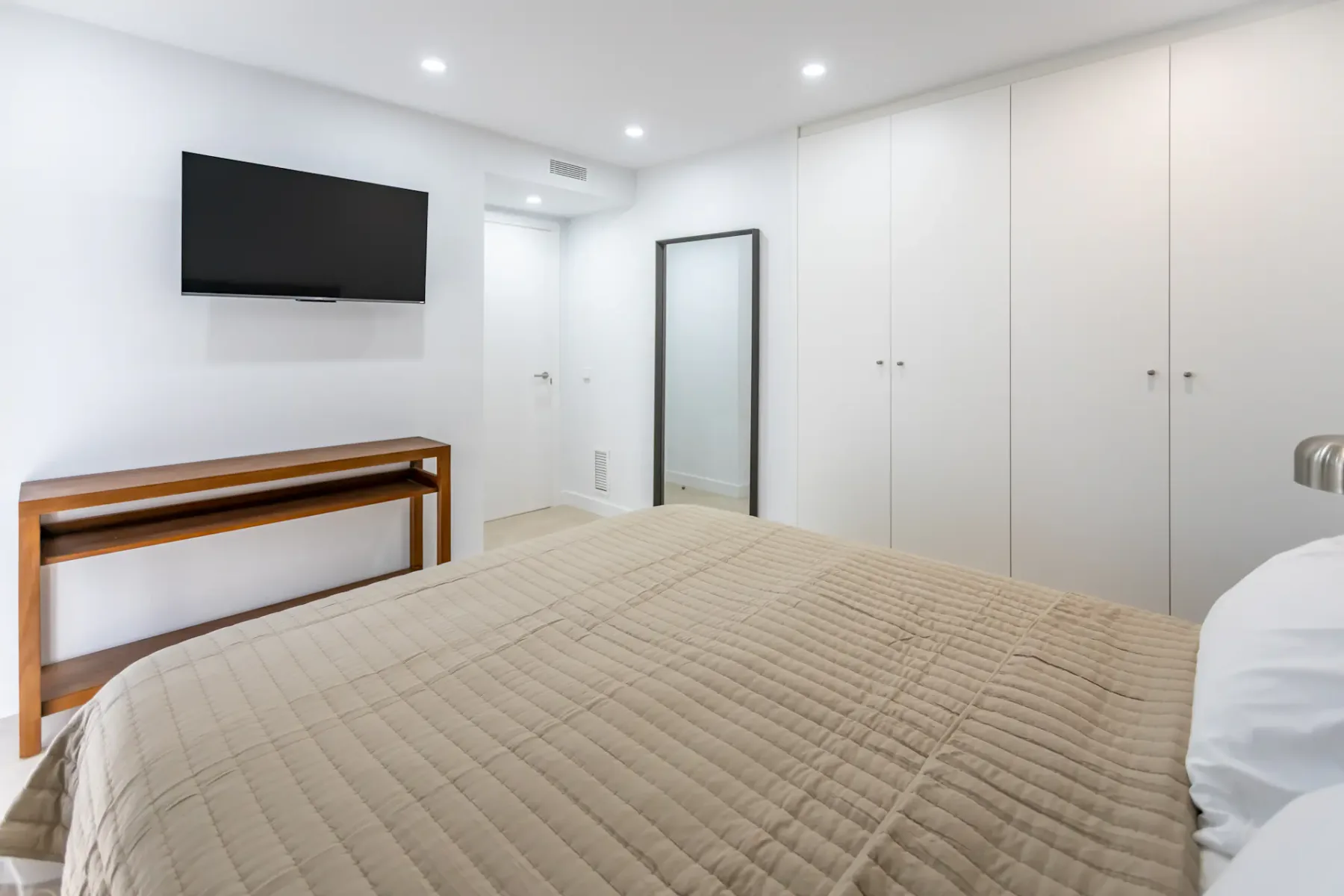 A bedroom with a bed, wall-mounted television, and built-in cabinets.