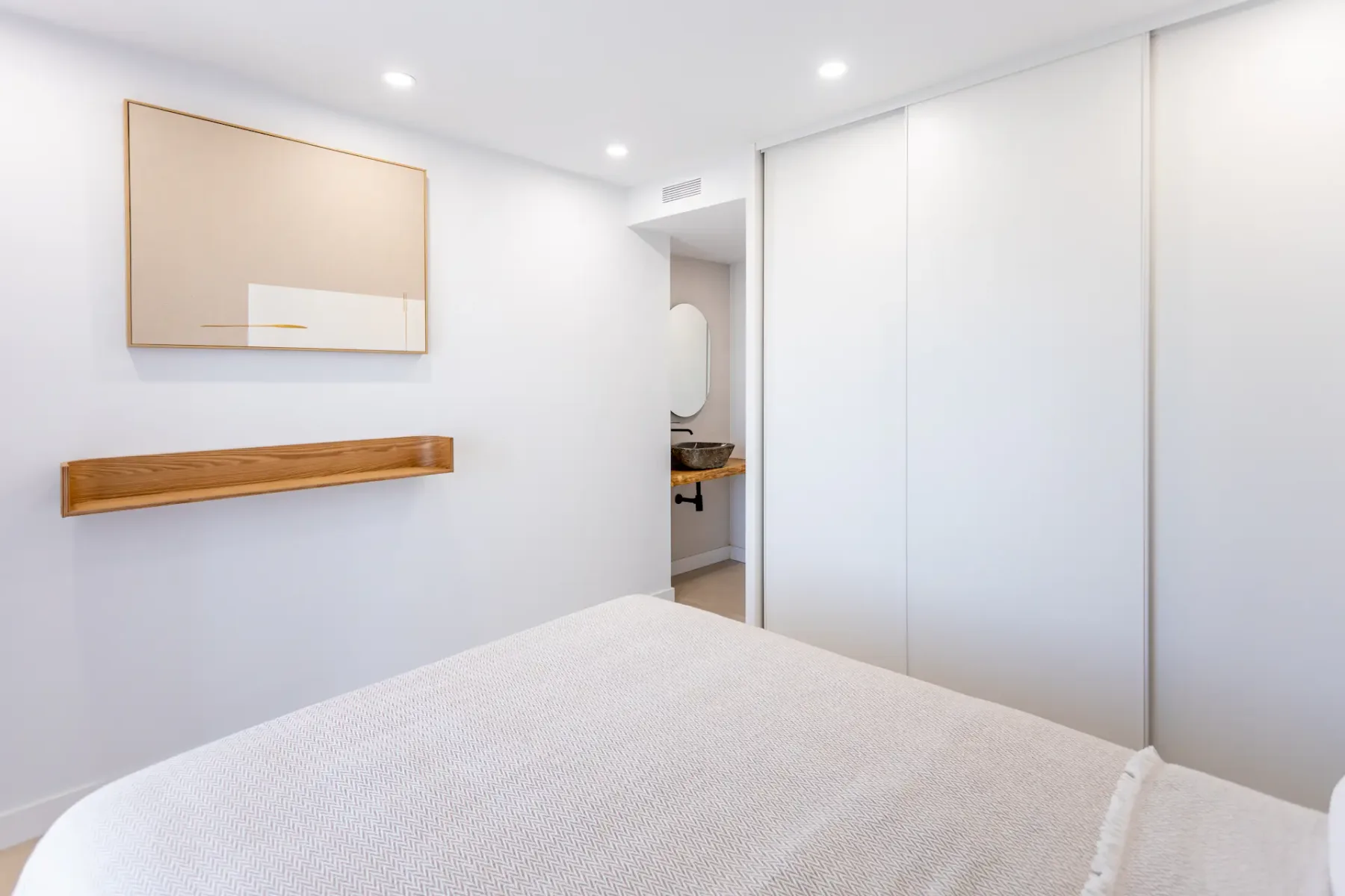 A bright bedroom with a bed and sliding white wardrobe doors.