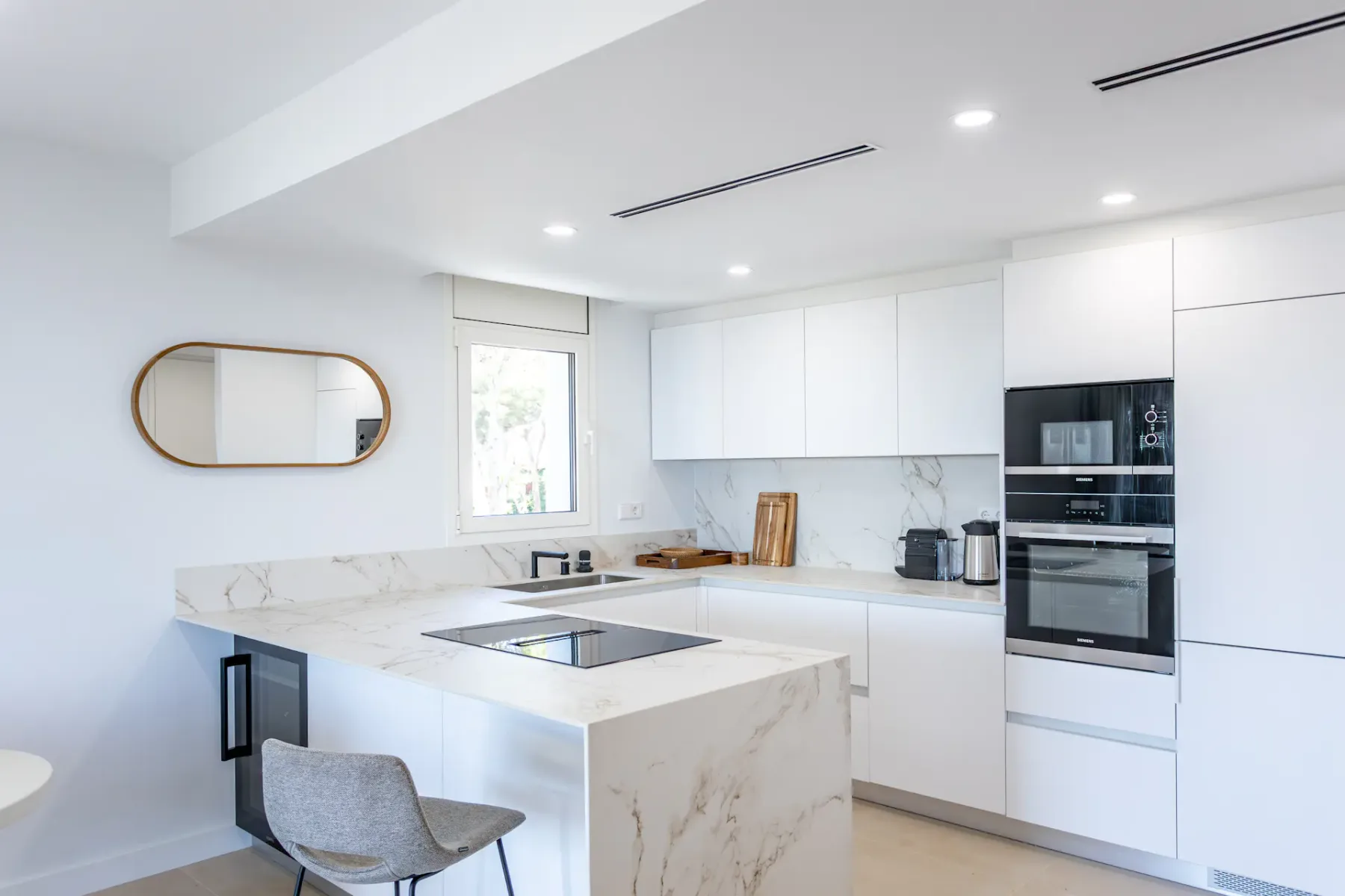 A bright modern kitchen with white cabinetry, a marble island, and built-in appliances.
