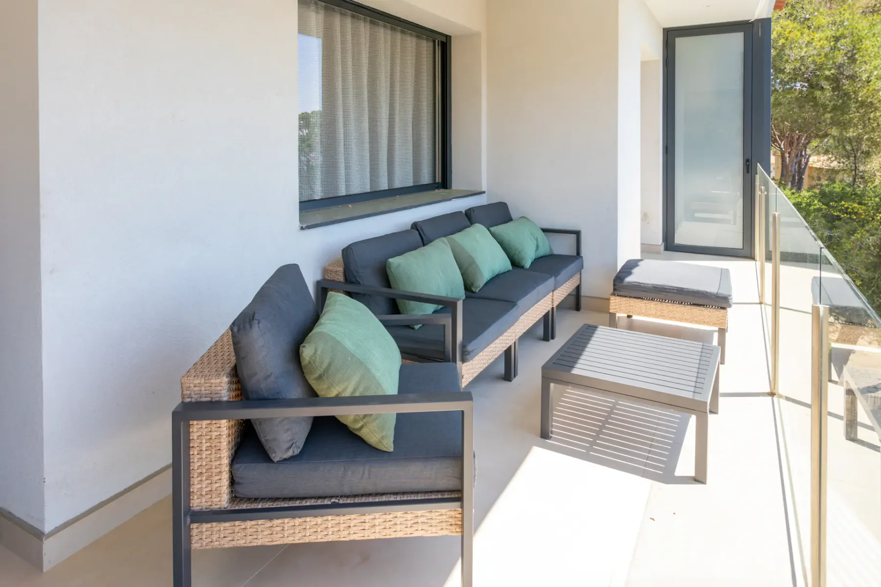 A bright outdoor seating area with cushioned lounge furniture beside a glass railing.