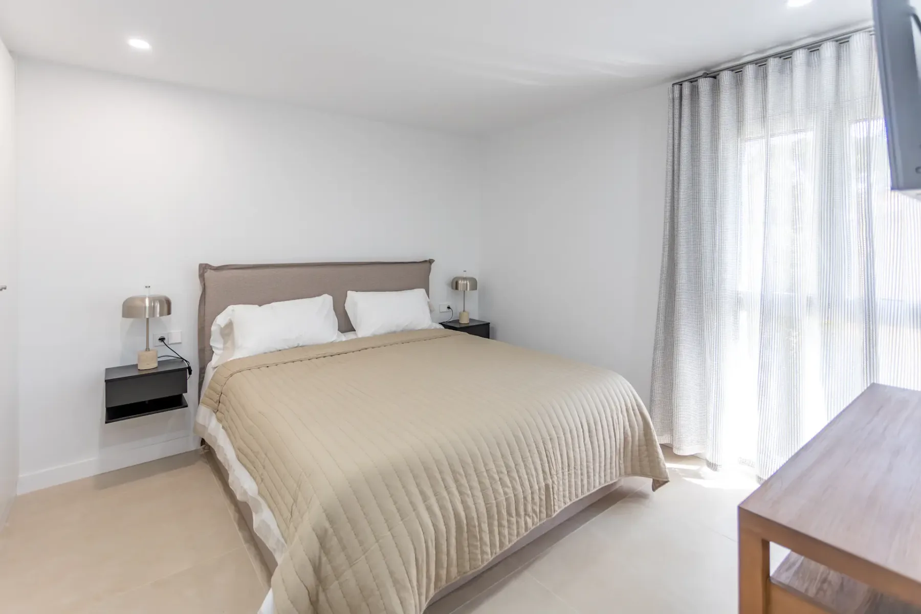 A bedroom with a neatly made bed and curtains beside a bright window.