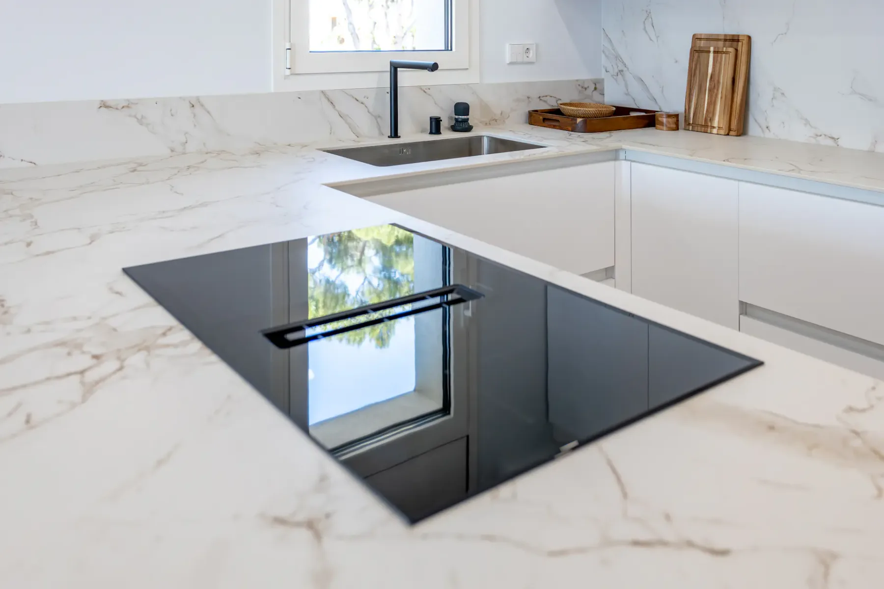 A modern kitchen with a black cooktop set into a pale countertop.