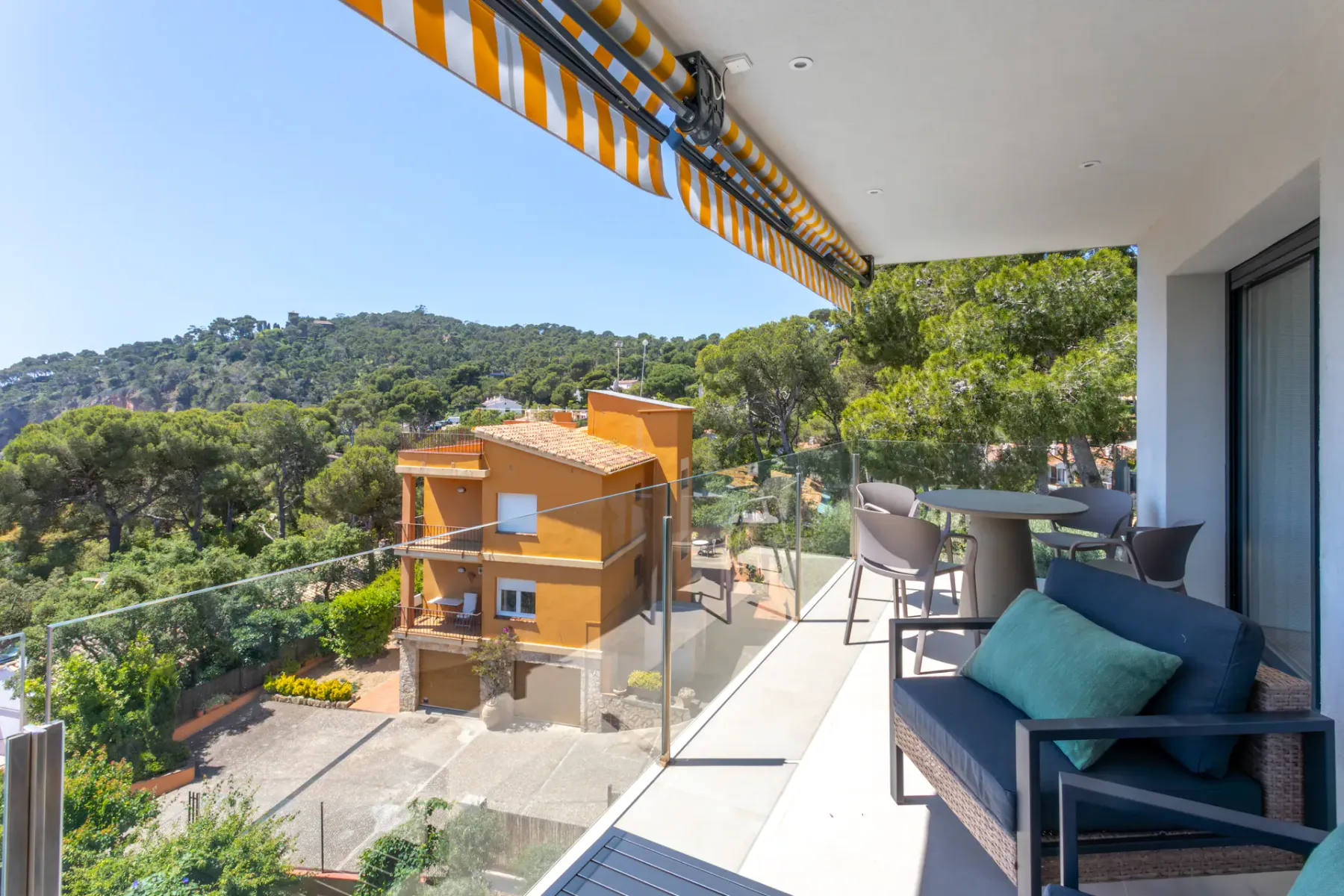 A balcony seating area overlooks a wooded hillside and nearby buildings.