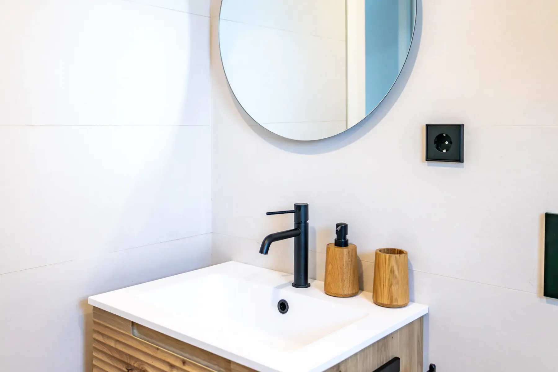 A bathroom vanity with a white basin, dark faucet, and round mirror.