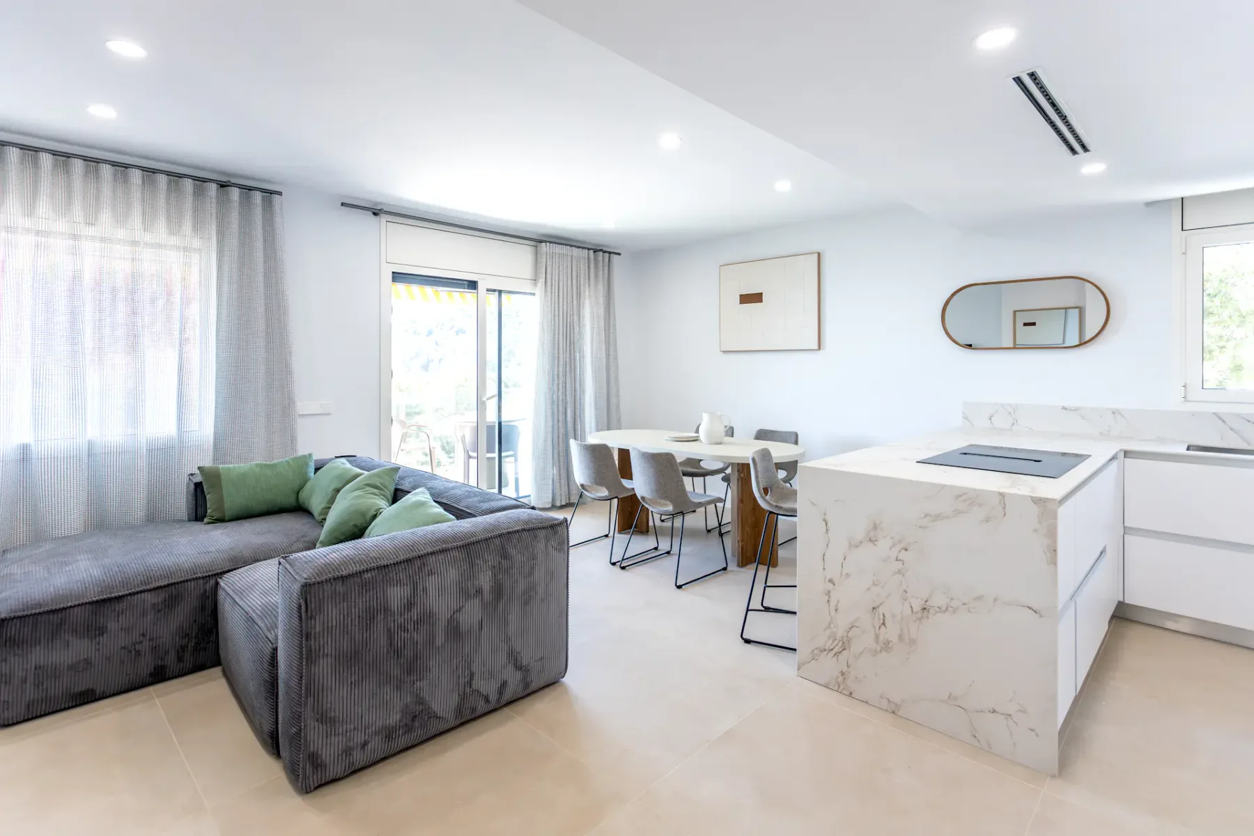 A bright open-plan living area has a gray seating area beside a kitchen island.
