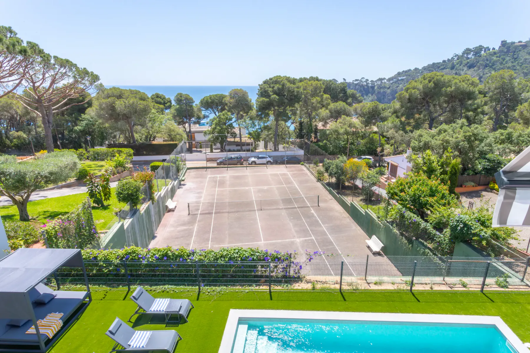 Shared amenity: A tennis court bordered by greenery, with a pool and lounge seating in the foreground.