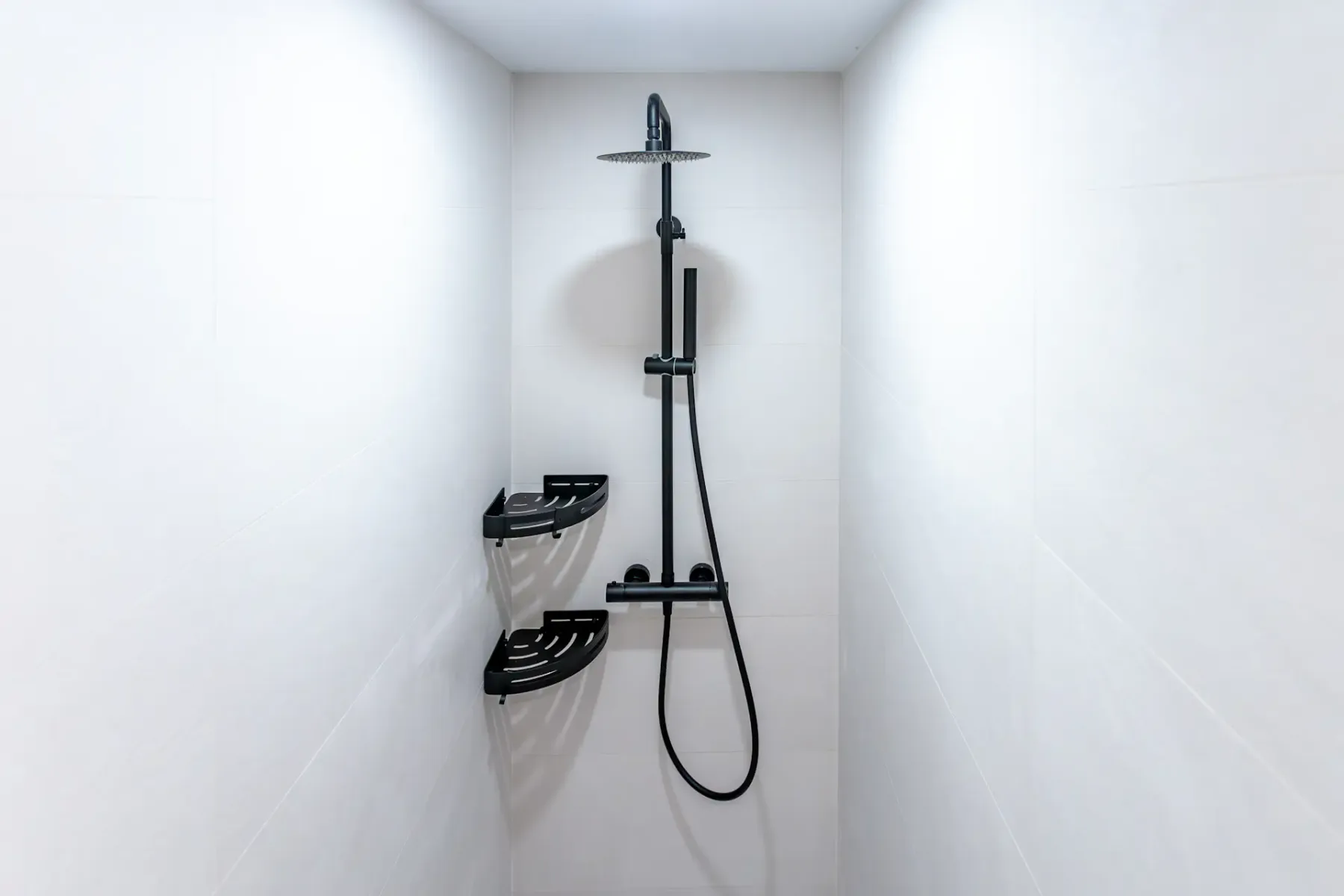 A tiled shower area with a dark shower fixture and corner shelves.