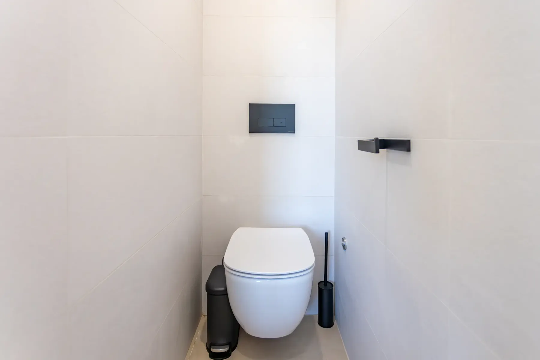 A compact bathroom with a toilet and wall-mounted flush panel.