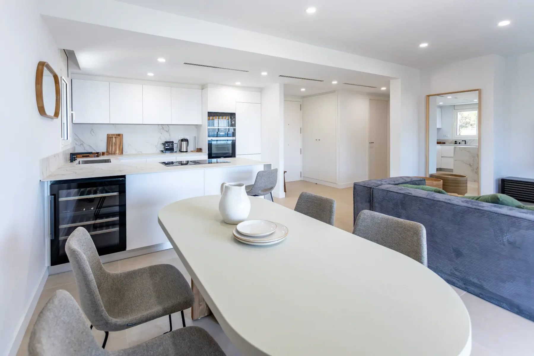 A bright open-plan kitchen and dining area with a long table and white cabinetry.