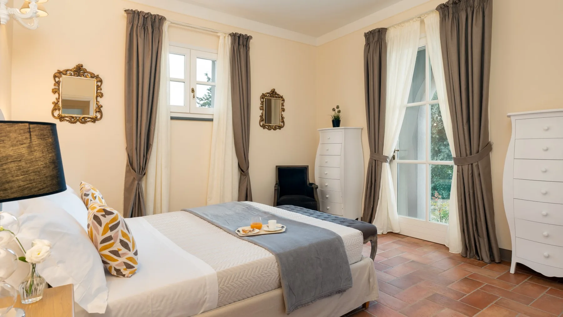 Un dormitorio con una cama bien tendida y ventanas altas con cortinas.